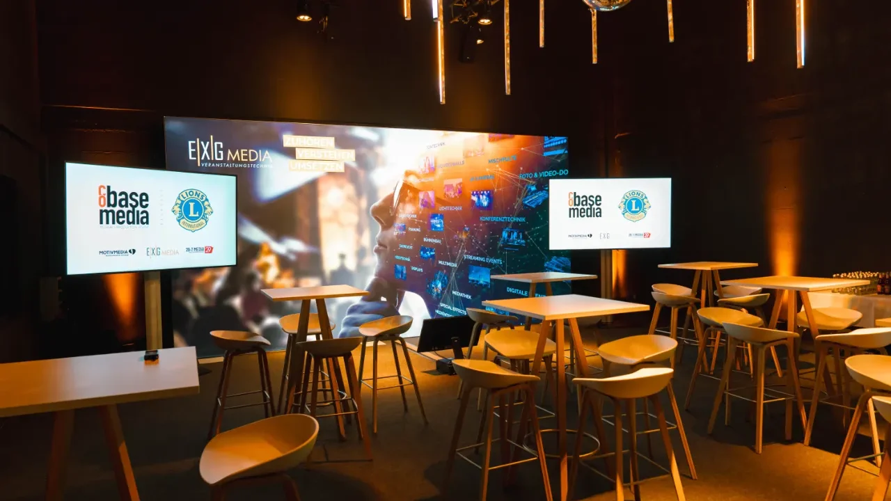 Eventlocation mit Backdrop, zwei Displays, Tischen und Bestuhlung.