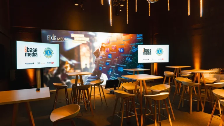 Eventlocation mit Backdrop, zwei Displays, Tischen und Bestuhlung.